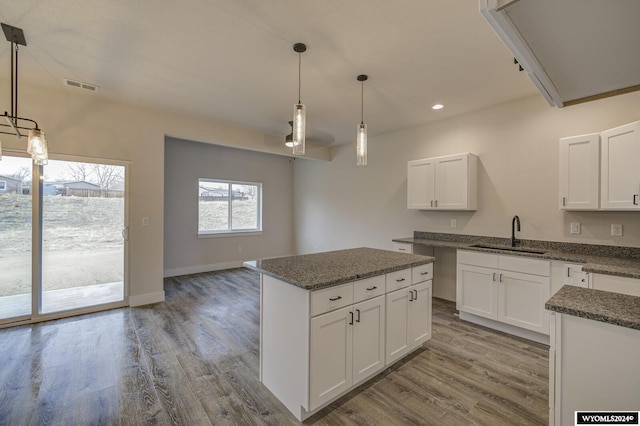 kitchen with a center island, sink, light wood-type flooring, decorative light fixtures, and white cabinetry