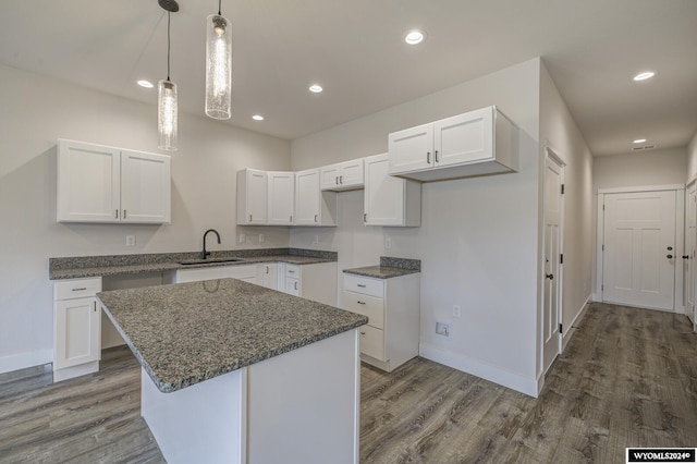 kitchen with a kitchen island, sink, wood-type flooring, white cabinetry, and hanging light fixtures