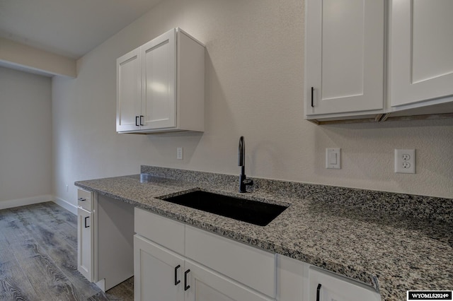 kitchen featuring white cabinets, light stone countertops, light wood-type flooring, and sink