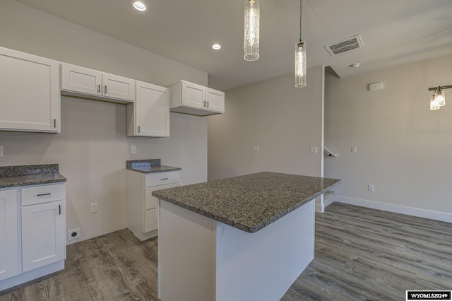 kitchen with wood-type flooring, white cabinetry, pendant lighting, and dark stone countertops