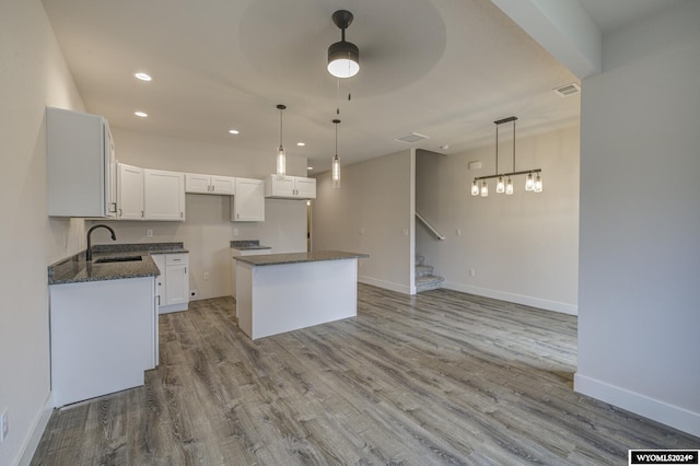 kitchen with light wood-type flooring, a kitchen island, sink, white cabinetry, and hanging light fixtures