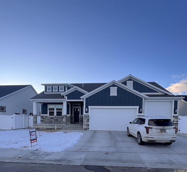 view of front facade featuring driveway, stone siding, fence, board and batten siding, and an attached garage