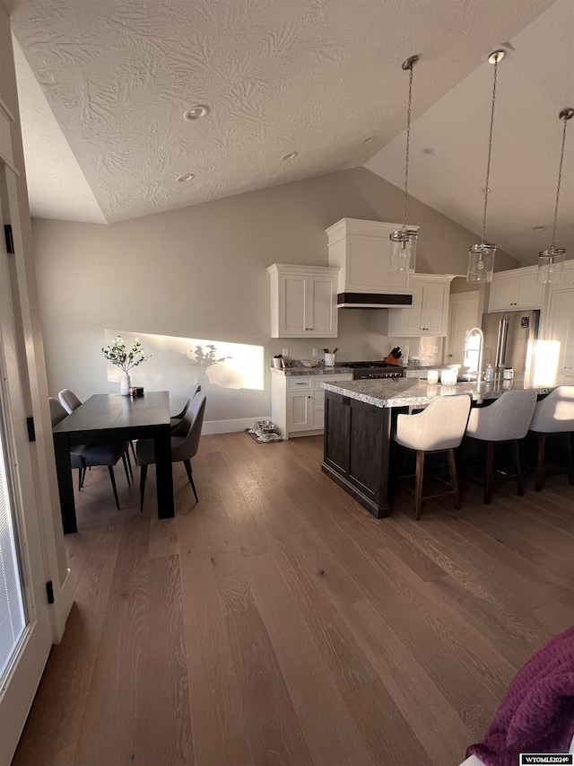 kitchen featuring a kitchen bar, dark wood finished floors, range hood, white cabinetry, and vaulted ceiling