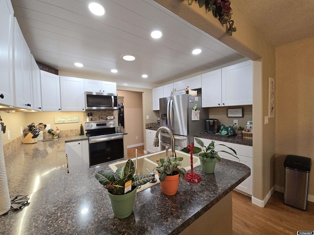 kitchen with light hardwood / wood-style flooring, dark stone countertops, appliances with stainless steel finishes, kitchen peninsula, and white cabinets