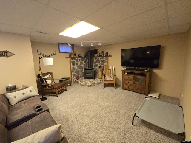 living room with a drop ceiling, track lighting, a wood stove, and carpet