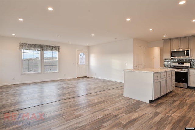 kitchen with a center island, backsplash, wood-type flooring, gray cabinets, and appliances with stainless steel finishes