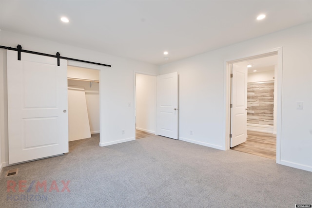 unfurnished bedroom featuring light colored carpet, a spacious closet, connected bathroom, and a closet