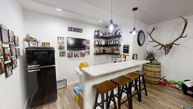 bar featuring black refrigerator, wood-type flooring, and hanging light fixtures