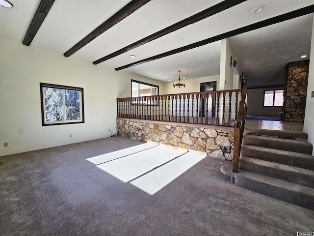 unfurnished living room featuring carpet flooring, beam ceiling, and an inviting chandelier