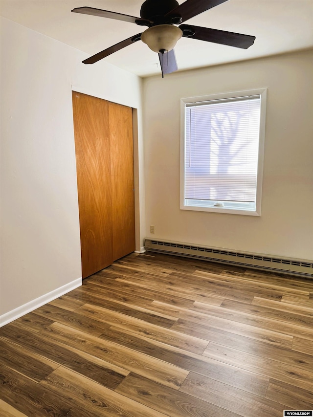 unfurnished bedroom with baseboard heating, ceiling fan, a closet, and wood-type flooring