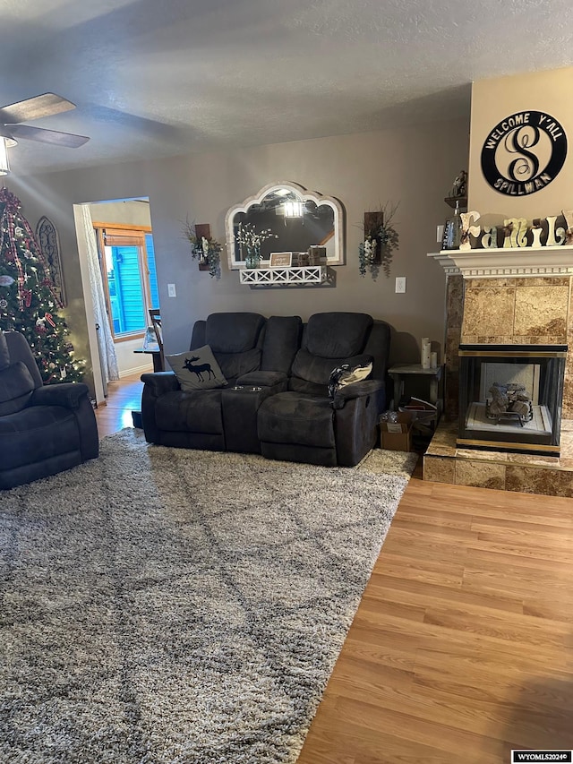 living room featuring a fireplace, a textured ceiling, hardwood / wood-style flooring, and ceiling fan