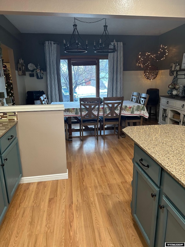 kitchen featuring pendant lighting, light wood-type flooring, light stone counters, and a notable chandelier