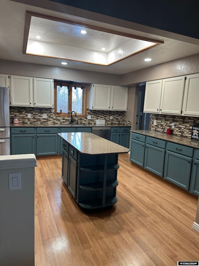 kitchen featuring stainless steel appliances, a kitchen island, a textured ceiling, white cabinets, and light wood-type flooring