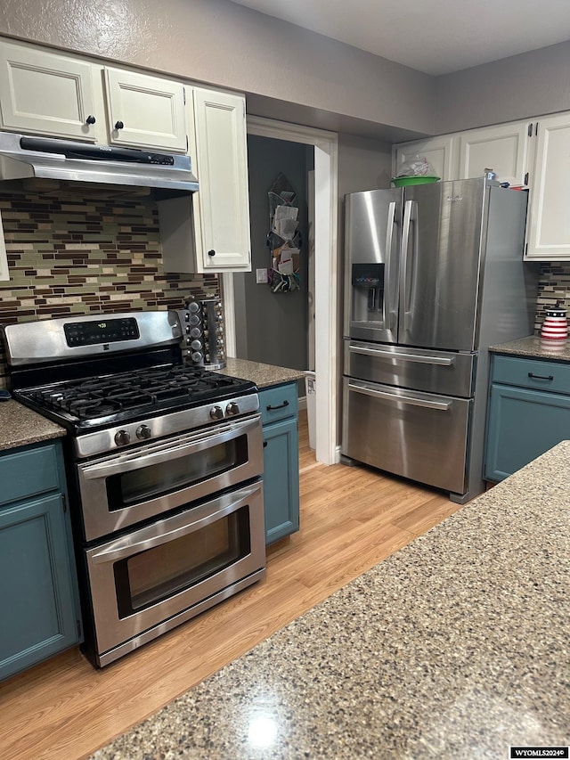 kitchen featuring white cabinets, blue cabinets, light wood-type flooring, appliances with stainless steel finishes, and tasteful backsplash