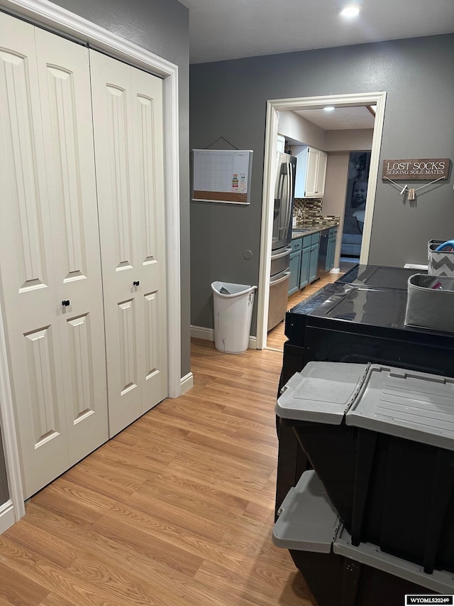 interior space with stainless steel fridge, backsplash, blue cabinets, light hardwood / wood-style flooring, and white cabinets