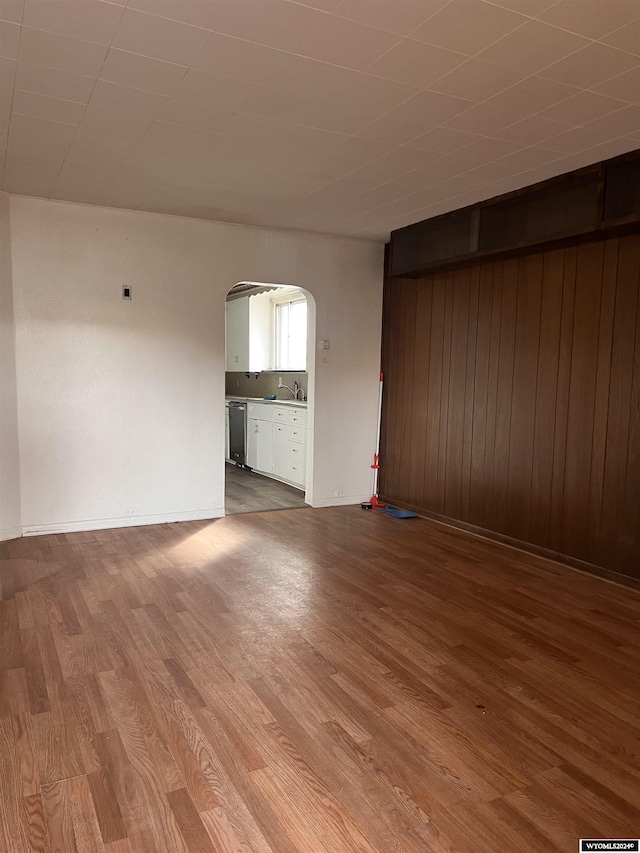 unfurnished living room with wood walls, sink, and hardwood / wood-style flooring