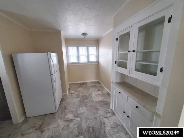 kitchen with a textured ceiling, white fridge, white cabinetry, and ornamental molding