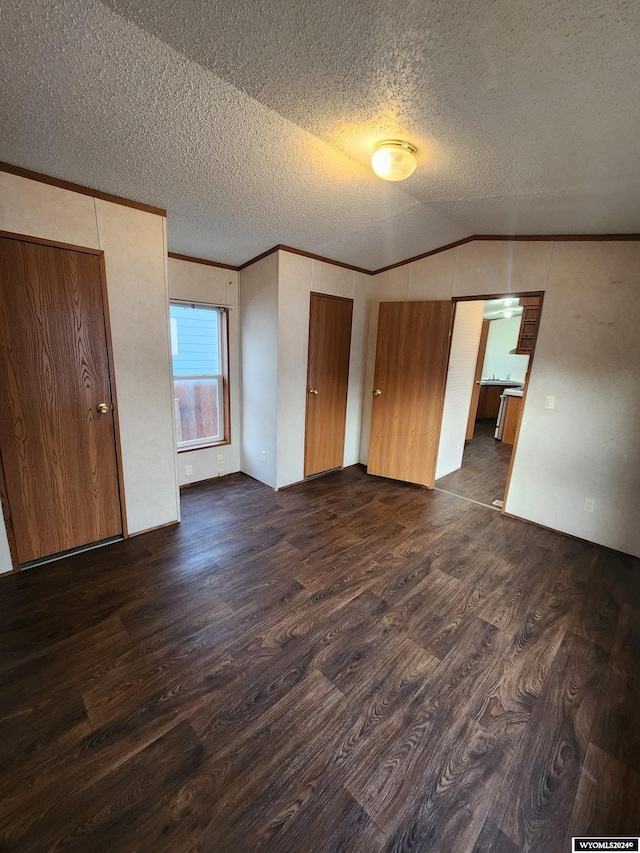 interior space featuring a textured ceiling, dark wood-type flooring, vaulted ceiling, and ornamental molding