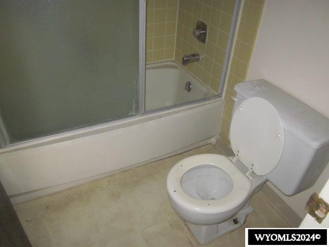 bathroom with toilet and bath / shower combo with glass door