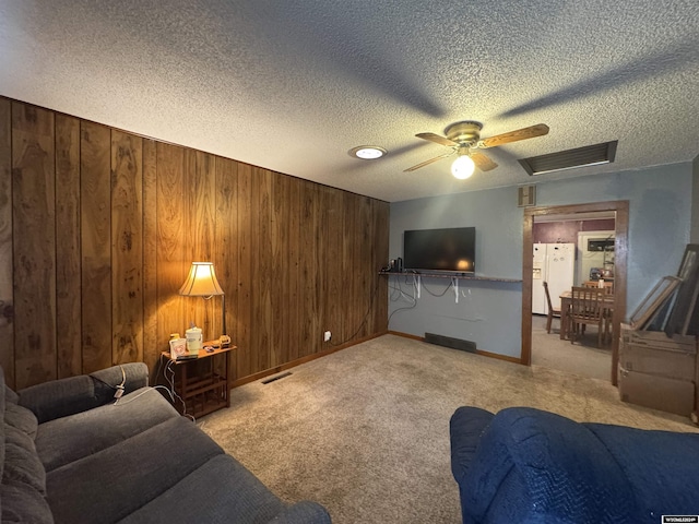 carpeted living room with wooden walls, ceiling fan, and a textured ceiling