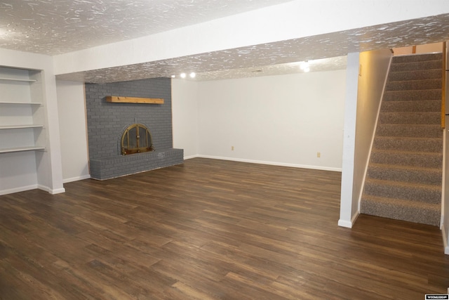 basement featuring built in features, a textured ceiling, dark hardwood / wood-style floors, and a brick fireplace