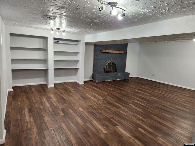 unfurnished living room featuring a textured ceiling, built in shelves, dark hardwood / wood-style floors, and a brick fireplace