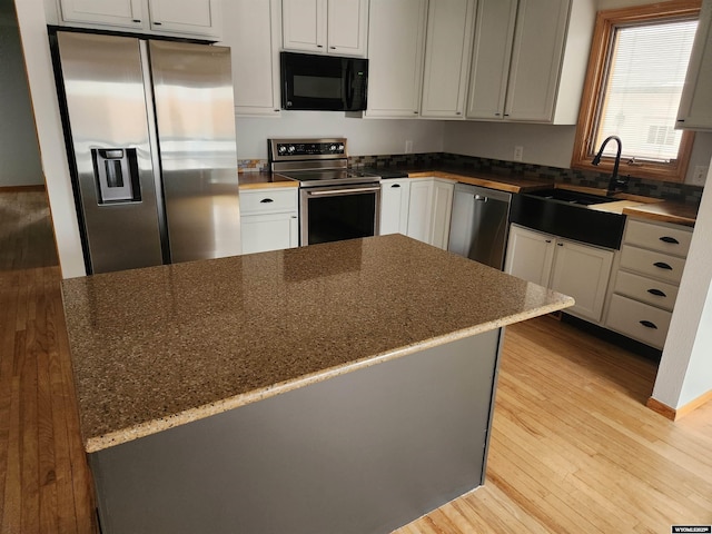 kitchen with appliances with stainless steel finishes, light wood-type flooring, dark stone counters, sink, and gray cabinets