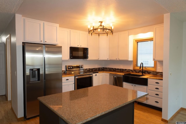 kitchen with a center island, stainless steel appliances, dark stone countertops, a chandelier, and white cabinets