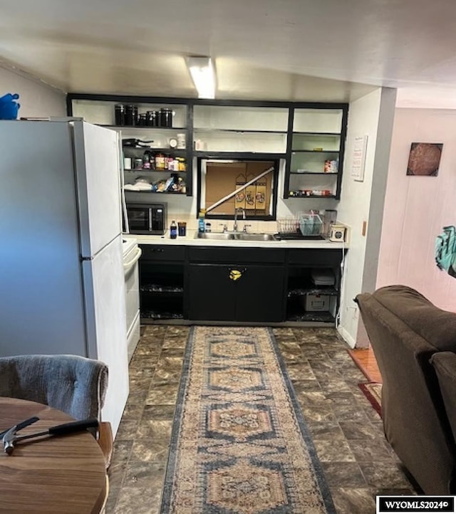 kitchen featuring open shelves, freestanding refrigerator, a sink, light countertops, and dark cabinets