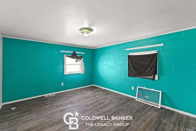 spare room with concrete block wall, wood finished floors, visible vents, and baseboards