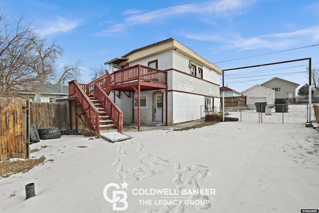 snow covered property featuring a wooden deck, stairs, an outdoor structure, and fence