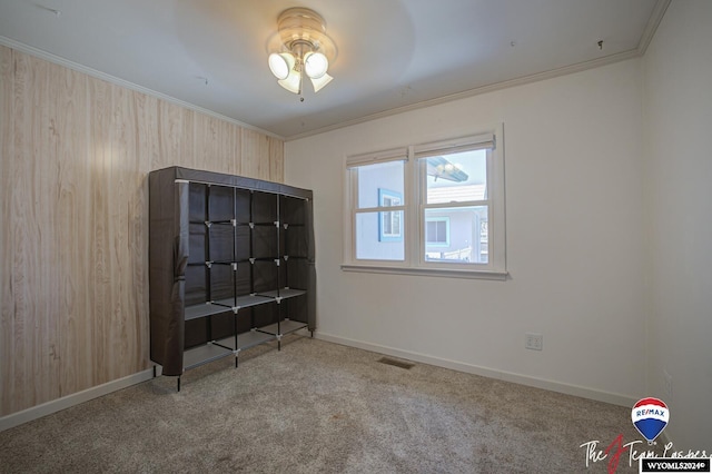 empty room with crown molding, carpet floors, and wood walls