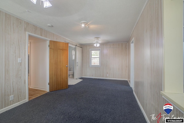 carpeted spare room with ceiling fan, ornamental molding, a textured ceiling, and wooden walls