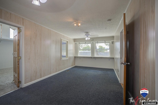 carpeted spare room with a textured ceiling, crown molding, ceiling fan, and wooden walls