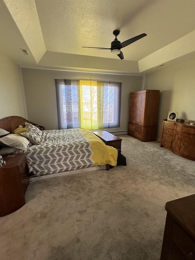 carpeted bedroom with a tray ceiling, ceiling fan, and a textured ceiling