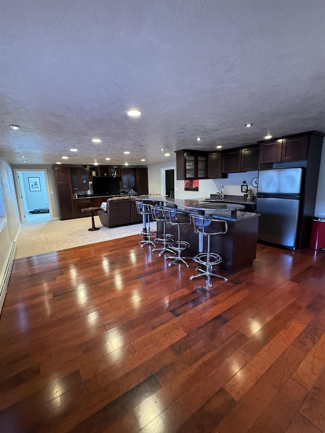 kitchen with dark wood-type flooring, a kitchen island, dark brown cabinetry, a breakfast bar area, and stainless steel refrigerator