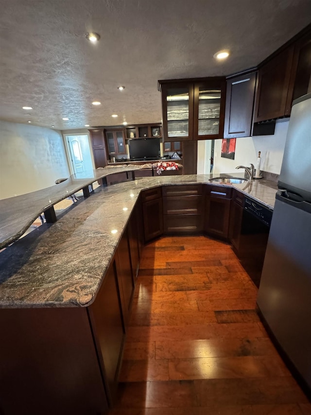 kitchen featuring light stone countertops, dark wood-type flooring, sink, black dishwasher, and stainless steel refrigerator