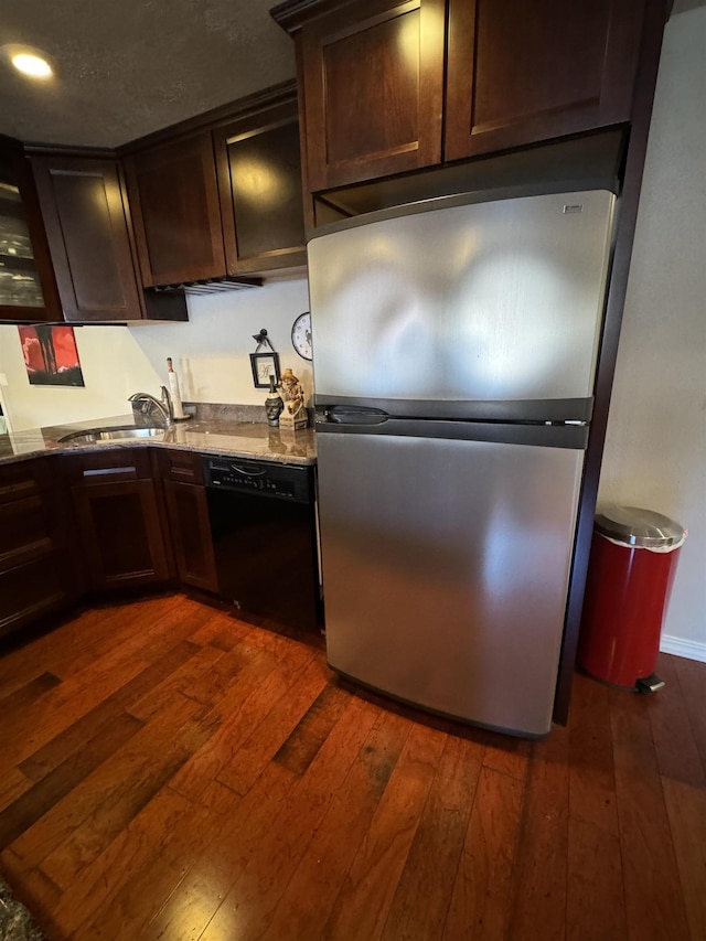 kitchen with light stone countertops, sink, black dishwasher, dark hardwood / wood-style floors, and stainless steel refrigerator