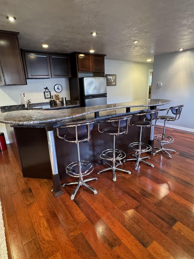 bar featuring stainless steel fridge, a textured ceiling, dark hardwood / wood-style floors, and dark brown cabinets