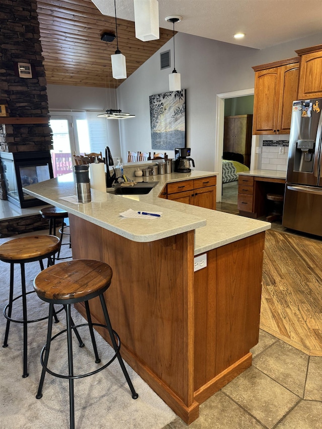 kitchen featuring hanging light fixtures, a kitchen breakfast bar, backsplash, stainless steel fridge, and lofted ceiling