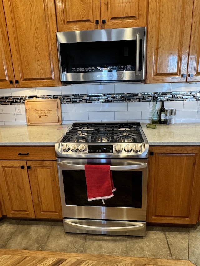 kitchen with light stone counters, appliances with stainless steel finishes, and tasteful backsplash