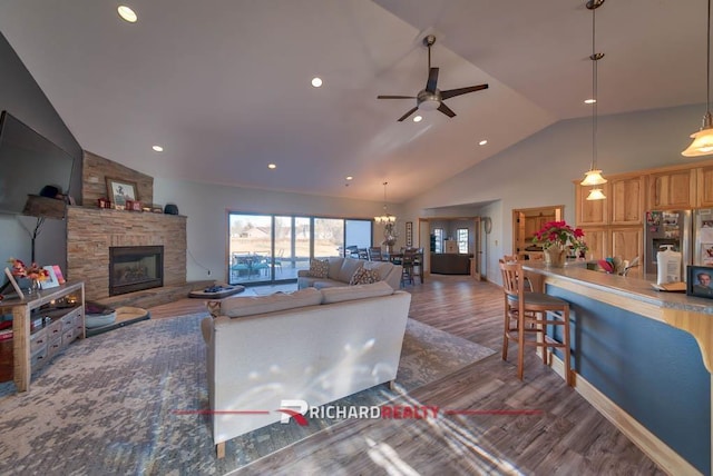 living room with ceiling fan with notable chandelier, a fireplace, dark wood-type flooring, and vaulted ceiling