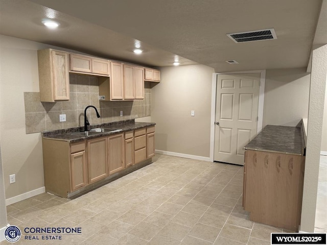 kitchen featuring backsplash, dark stone countertops, sink, and light brown cabinetry