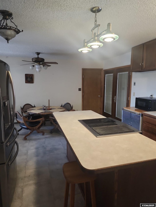 kitchen with a breakfast bar, stainless steel refrigerator with ice dispenser, ceiling fan, a textured ceiling, and decorative light fixtures