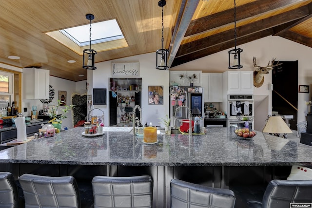 kitchen featuring vaulted ceiling with skylight, white cabinetry, wood ceiling, and dark stone counters