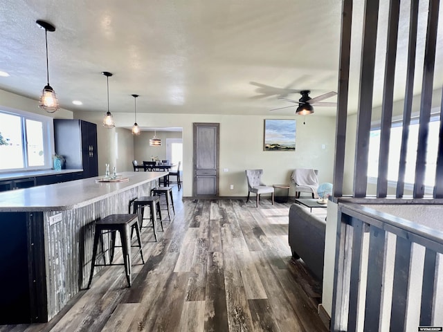 kitchen with a breakfast bar, ceiling fan, decorative light fixtures, a kitchen island, and dark hardwood / wood-style flooring