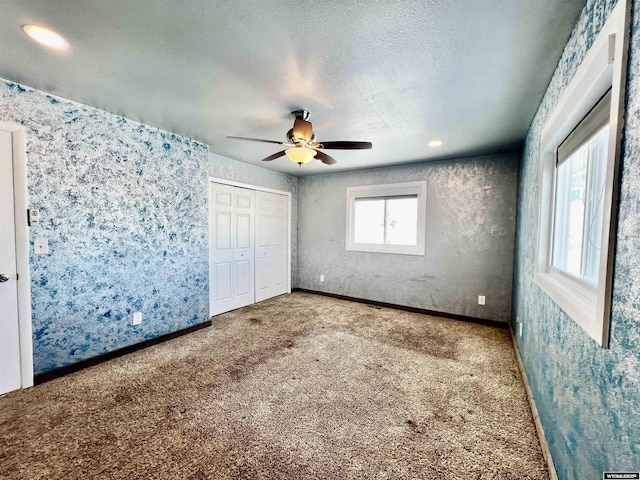 unfurnished bedroom featuring carpet, a textured ceiling, a closet, and ceiling fan