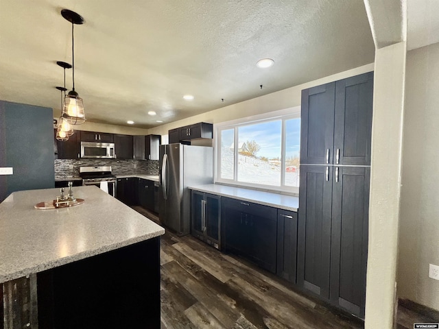 kitchen featuring tasteful backsplash, a textured ceiling, stainless steel appliances, dark wood-type flooring, and hanging light fixtures