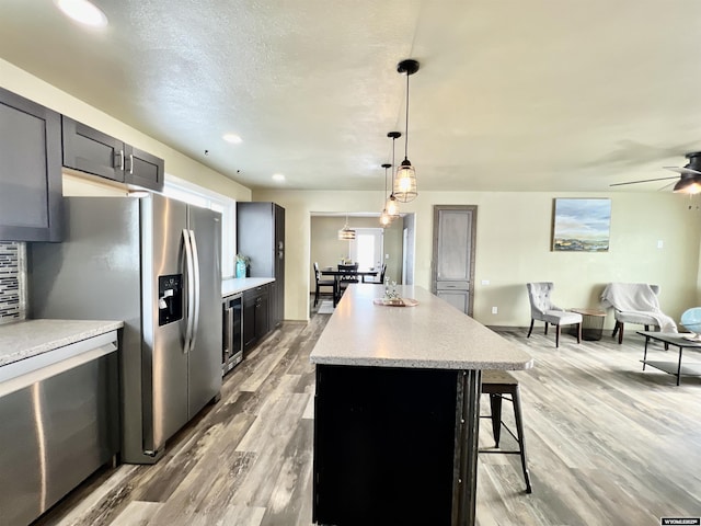 kitchen featuring ceiling fan, beverage cooler, hanging light fixtures, light hardwood / wood-style floors, and a kitchen island