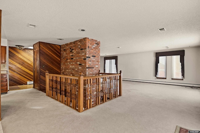 hall featuring light carpet, a textured ceiling, wooden walls, and baseboard heating